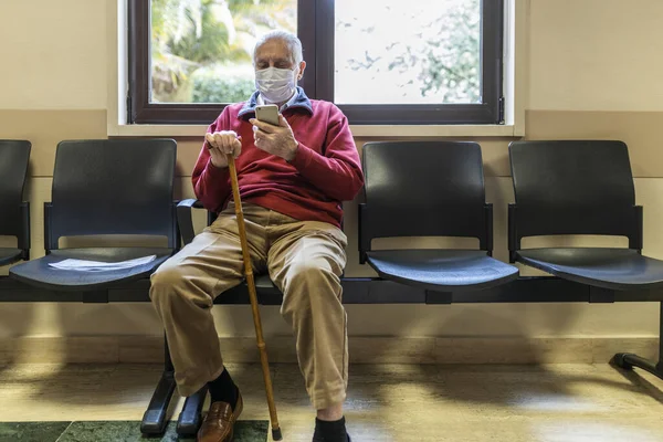 Doktorun ofisinde solunum cihazıyla oturan ve akıllı telefonunu kullanan yaşlı bir adam.