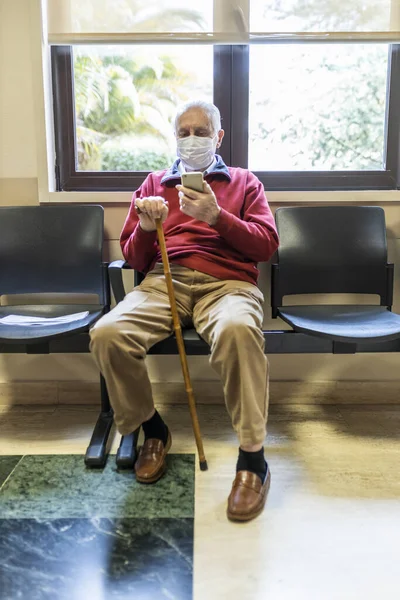 老年人坐在一家医院的医生办公室里 拿着呼吸器 用智能手机 — 图库照片