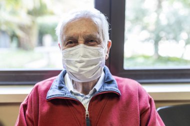 Doktorun muayenehanesinde solunum cihazıyla oturan yaşlı adam, kameraya bak.