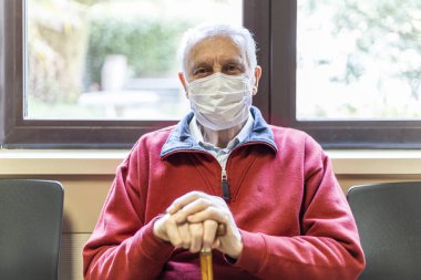 Doktorun muayenehanesinde solunum cihazıyla oturan yaşlı adam, kameraya bak.