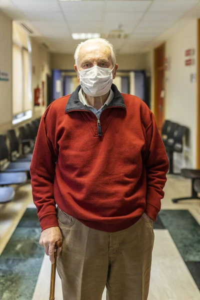 Elderly man walking down a corridor of medical consultation in a hospital with respirator, front view