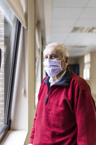 Elderly man near the window of the medical consultation in a hospital with a respirator, look at camera