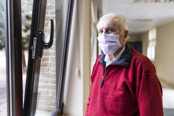 Elderly man near the window of the medical consultation in a hospital with a respirator, look at camera