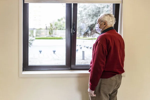 Elderly man looking out the window of the medical consultation in a hospital with a respirator.