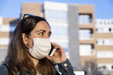 Genç bir kadın sokakta solunum cihazıyla akıllı telefonuyla konuşuyor.