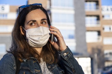 Genç bir kadın sokakta solunum cihazıyla akıllı telefonuyla konuşuyor.