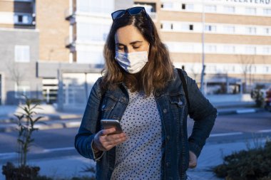 Genç bir kadın sokakta solunum cihazıyla akıllı telefonuyla sohbet ediyor.