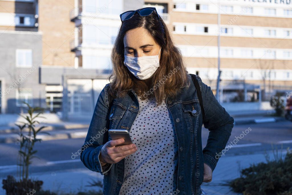 young woman chatting on her smart phone with a respirator on the street