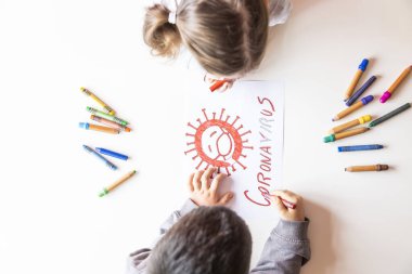 Tanımlanamayan kız ve erkek, beyaz bir masaya Coronavirus 'un resmini çiziyor.
