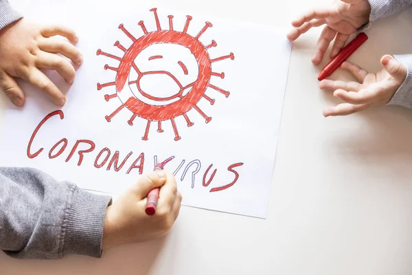 Unrecognizable boy and girl color a drawing of stop coronavirus on a white table, top view