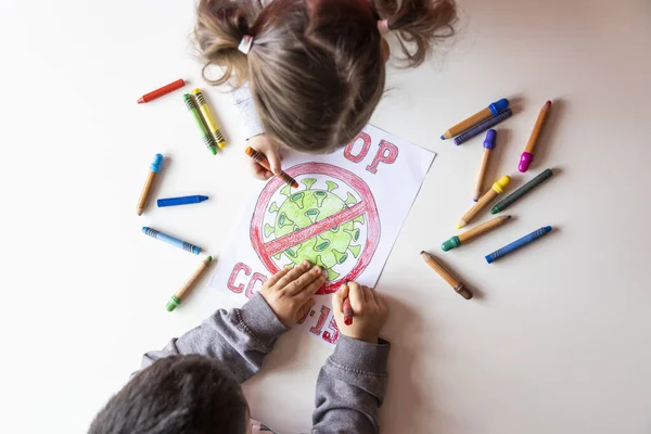 Unrecognizable boy and girl color a drawing of stop coronavirus on a white table, top view