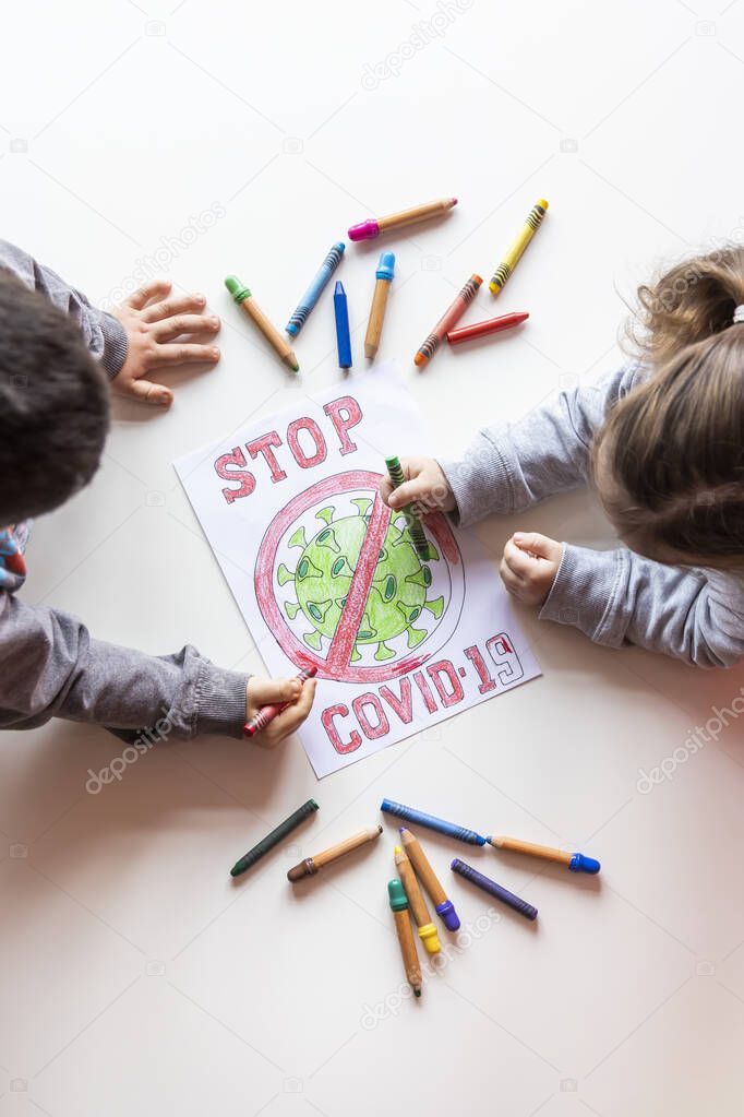 Unrecognizable boy and girl color a drawing of stop coronavirus on a white table, top view