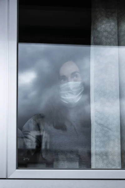 Kvinna Med Respirator Och Smart Telefon Tittar Genom Fönstret Hennes — Stockfoto