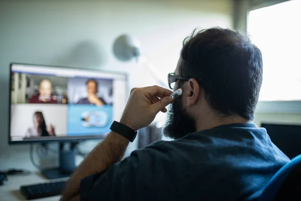 Sakallı adam 3 kişiyle video bağlantısı kuruyor ve akıllı telefon ve kulaklık kullanıyor.