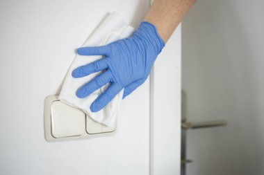 Tanımlanamayan bir kadın evinin yüzeyini dezenfekte ediyor, elektrik düğmelerini dezenfekte ediyor.