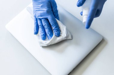 Tanımlanamayan bir kadın evinin yüzeyini dezenfekte ediyor, laptopunu dezenfekte ediyor.