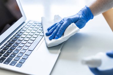 Tanımlanamayan bir kadın evinin yüzeyini dezenfekte ediyor, dizüstü bilgisayarını dezenfekte ediyor.