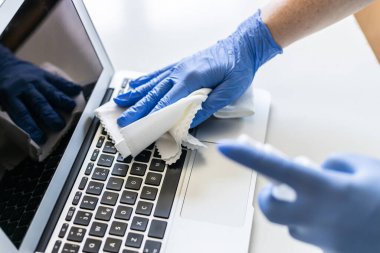 Tanımlanamayan bir kadın evinin yüzeyini dezenfekte ediyor, dizüstü bilgisayarını dezenfekte ediyor.