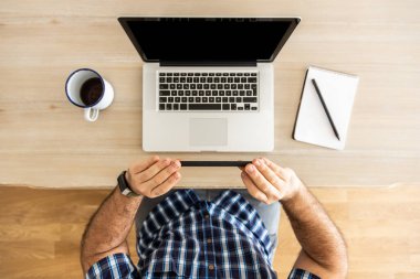 Tanımlanamayan bir adam evde dizüstü bilgisayarı, defteri ve bir fincan kahveyle çalışıyor. Telefonla fotoğraf çekiyor.