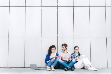 Kitaplar ve duvarın yanında katta oturan becerikli olan insanlar. Eğitim sosyal medya kavramı.