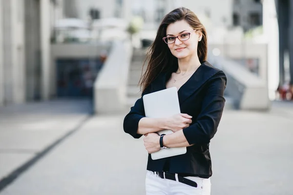 Mujer de negocios con un portátil de pie en una calle de una ciudad moderna — Foto de Stock