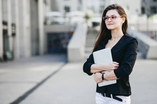 Mujer de negocios con un portátil de pie en una calle de una ciudad moderna — Foto de Stock