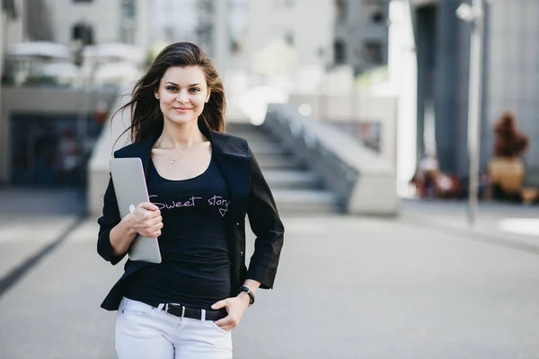 Mulher de negócios com um laptop em pé em uma rua em uma cidade moderna — Fotografia de Stock