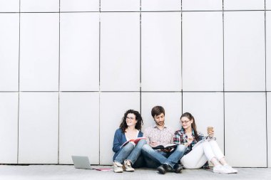 Kitaplar ve duvarın yanında katta oturan becerikli olan insanlar. Eğitim sosyal medya kavramı.
