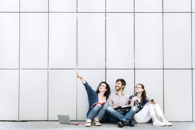 Genç insanlar, metin için boş bir alan üzerinde gösterilen gülümseyen ve oturan duvara yakın. Öğrenciler çalışıyorlar. Eğitim sosyal medya kavramı.