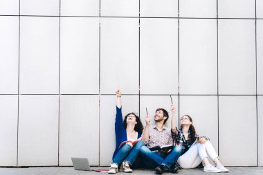 Genç insanlar, metin için boş bir alan üzerinde gösterilen gülümseyen ve oturan duvara yakın. Öğrenciler çalışıyorlar. Eğitim sosyal medya kavramı.