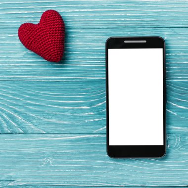 Smartphone ile beyaz perde ve güzel mavi ahşap arka plan üzerinde örme kalp. Sevgililer günü kavramı
