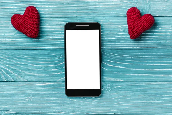 Smartphone ile beyaz perde ve güzel mavi ahşap arka plan üzerinde örme kalp. Sevgililer günü kavramı