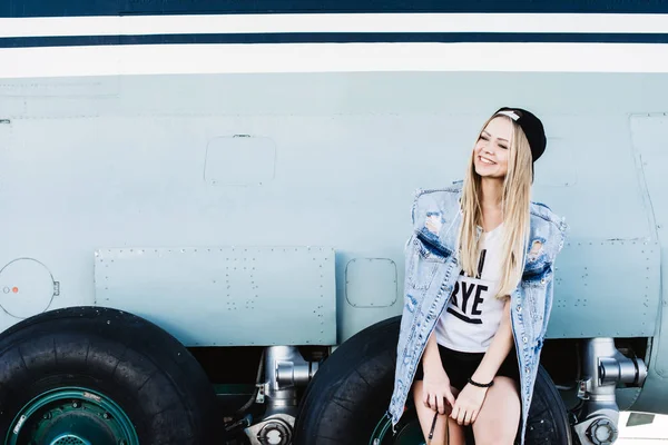 Mooie toeristische meisje poseren en zittend op vliegtuig wielen — Stockfoto