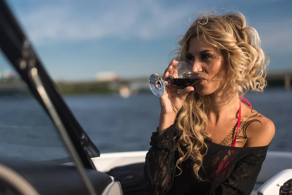 Portrait of attractive woman relaxing on yacht enjoying glass of wine on blue sky sea outdoors. Enjoyment and luxury lifestyle