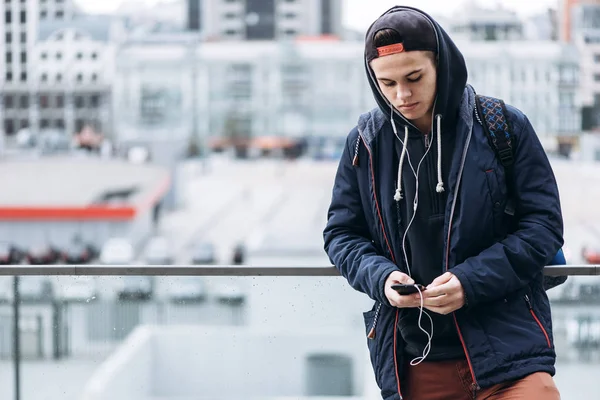 Teenage Boy Listening To Music And Using Phone In Urban Setting