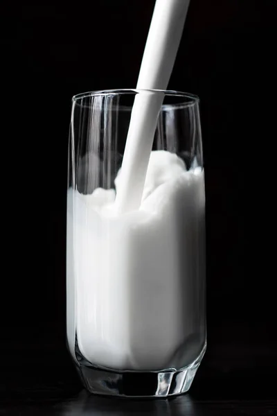 Pouring milkg in to a glass on the black background — Stock Photo, Image