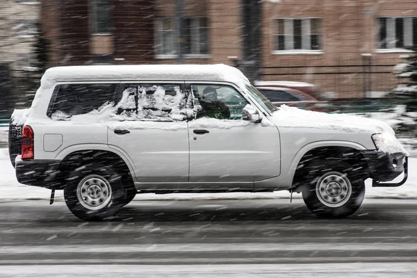 Weißer großer Geländewagen, der im Winter im Schneetreiben auf der Straße unterwegs ist — Stockfoto