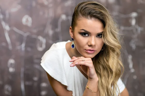 Menina loira bonita vestindo um vestido branco e jóias sentadas em uma cadeira — Fotografia de Stock