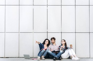Kitaplar ve duvarın yanında katta oturan becerikli olan insanlar. Eğitim sosyal medya kavramı.