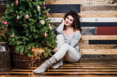 Bir Noel ağacı olan bir arka planda katta oturan güzel duygusal bir kız portresi. Noel ve yeni yıl kavramı.