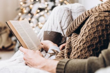 Bir kitap ve bir fincan sıcak bir Noel ağacı arka plan elinde içki. Noel ve yeni yıl kavramı