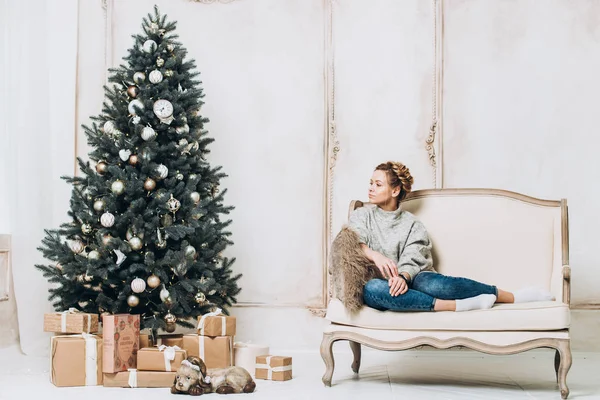Noel ağacının yanında oturan güzel kız. Yeni yıl kutlama. Güzel holdiay Oda ile altında bu hediyeleri Noel ağacı ile dekore edilmiştir. Yeni yıl ve Noel kavramları.