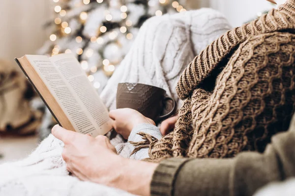 Bir kitap ve bir fincan sıcak bir Noel ağacı arka plan elinde içki. Noel ve yeni yıl kavramı