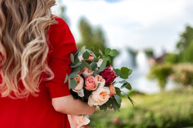 A blond woman with curly hair is holding a beautiful colored bouquet in her hands, with her back to the camera