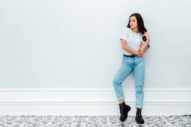 Pretty girl posing leaning against a white wall. Place for advertising