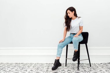 Stüdyoda beyaz duvarda bir sandalyede oturan güzel kız