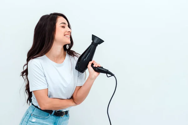 Mooi meisje met lang donker haar houdt een haardroger op een witte achtergrond — Stockfoto