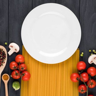 On a dark background stands a plate, pasta, tomatoes, spices