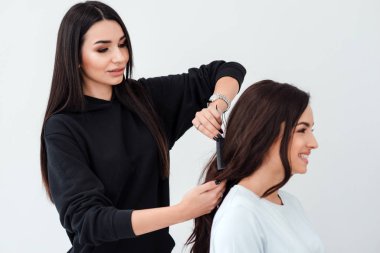 Beautiful, professional stylist makes a hairstyle for her lovely client