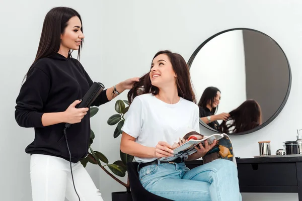 Parrucchiere donna felice facendo acconciatura per giovane ragazza. Nel corso del lavoro, una ragazza carina chiede qualcosa al maestro. . — Foto Stock